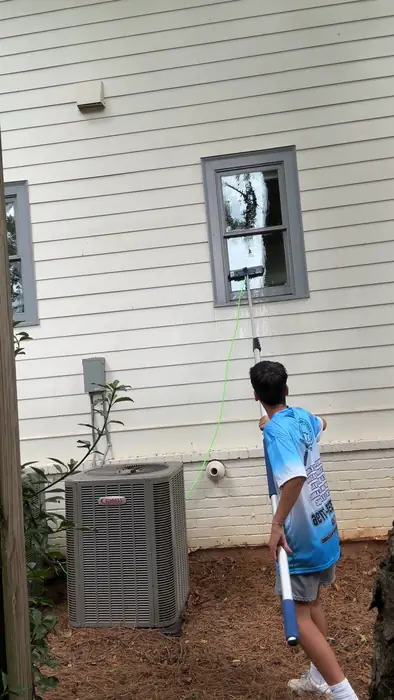 Crew member in a Kash's Window Washing shirt cleaning a second story window with a water fed pole