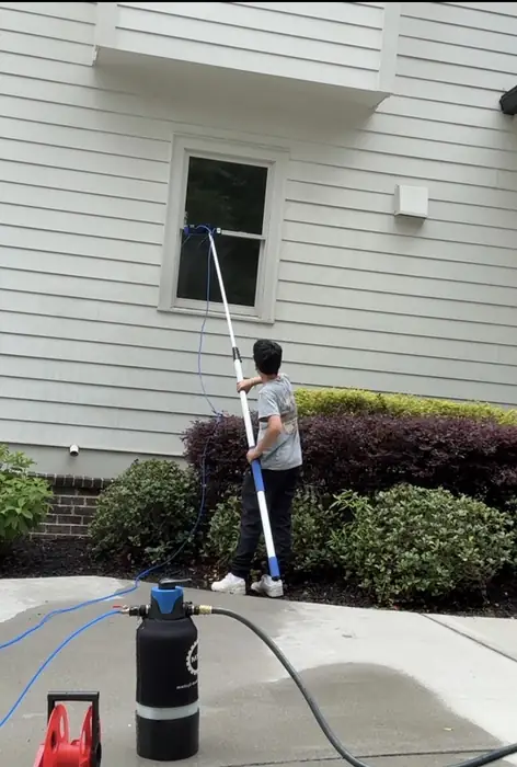 Crew member cleaning windows on a white home with a water fed pole and tank