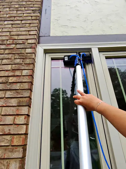 Step 1, Scrub: Pure water pole scrubbing a tall window on a brick home