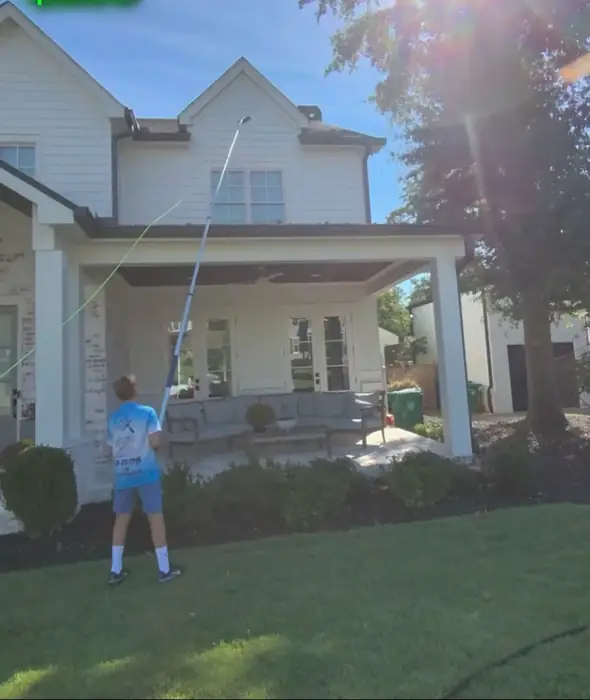 Crew member cleaning windows on a large two story white home